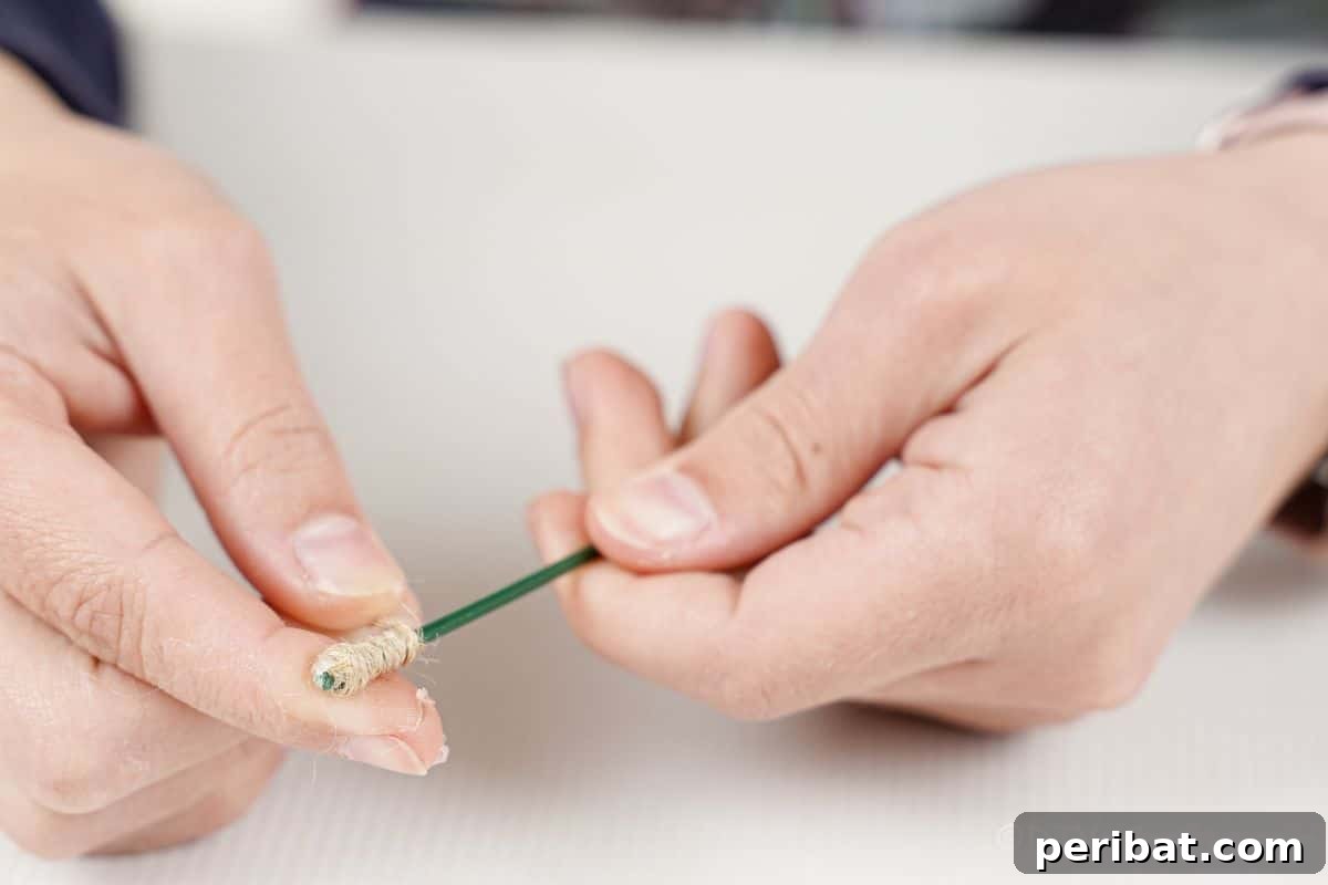 Hand holding a piece of floral wire with twine neatly wrapped around one end, starting a handle.