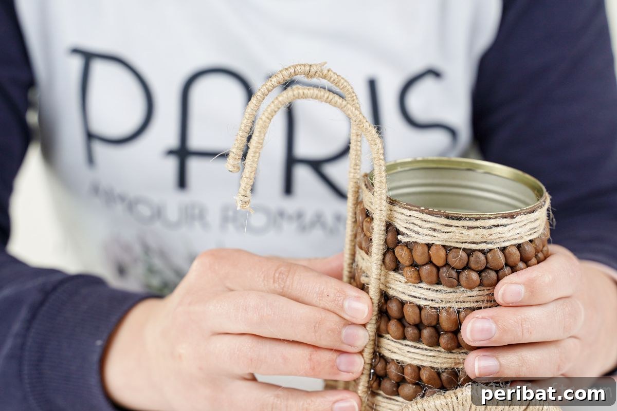 Twine handles being carefully held in place on the back of the tin can while glue dries.