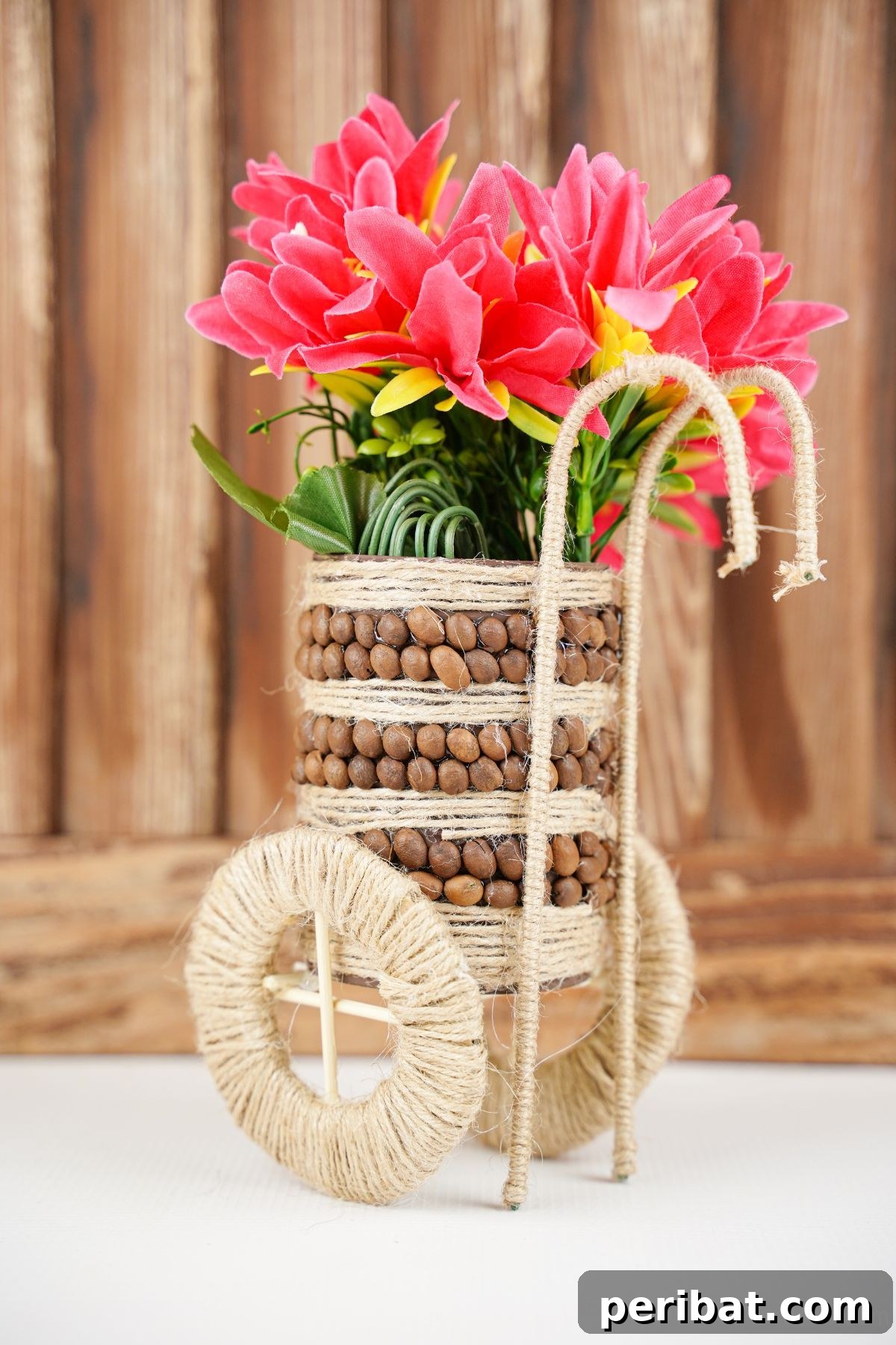 Close-up of a tin can vase decorated with coffee beans and twine, set against a warm wooden wall.