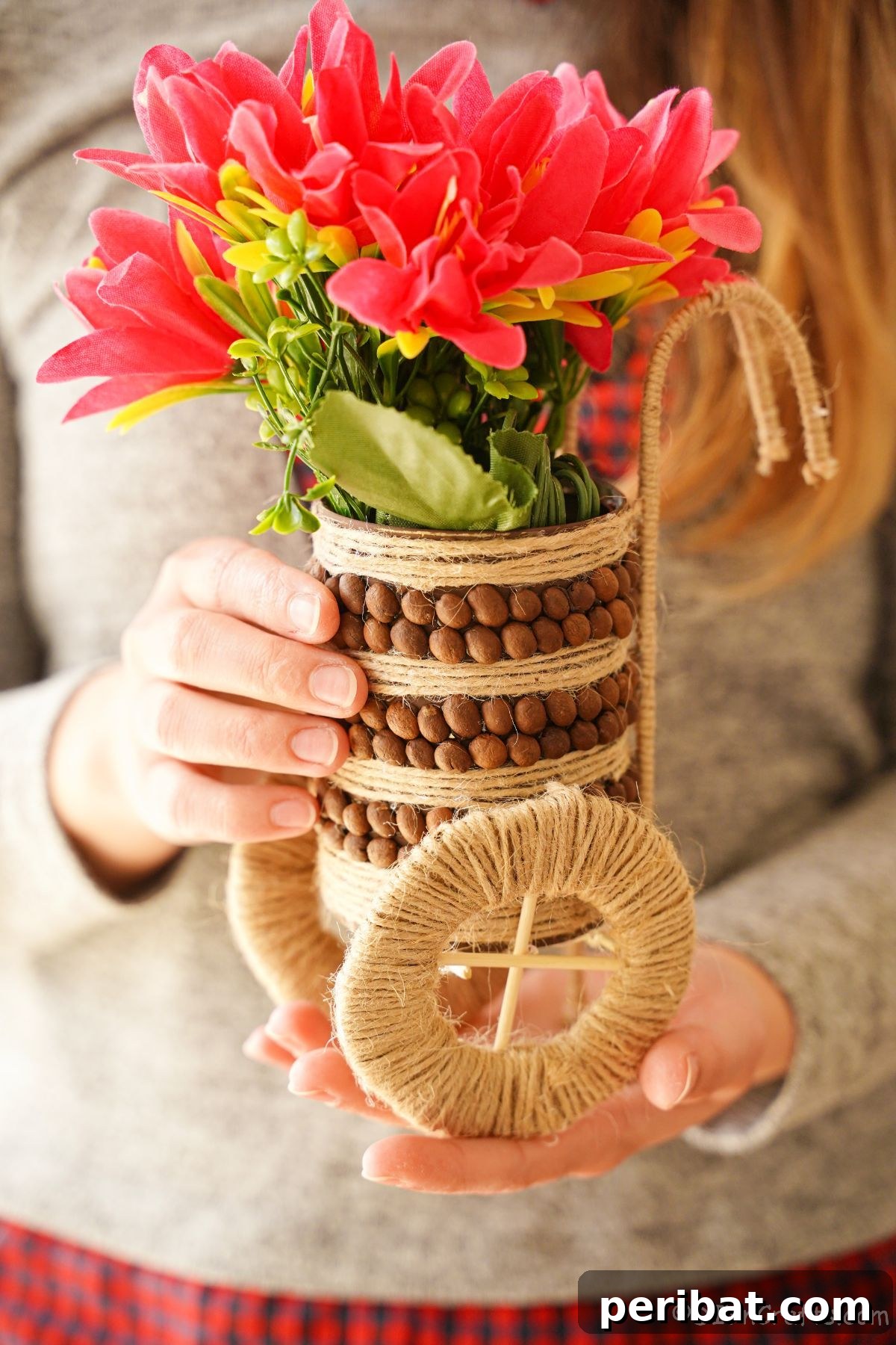 Lady holding a finished upcycled tin can vase with twine and coffee beans, showcasing the rustic design.