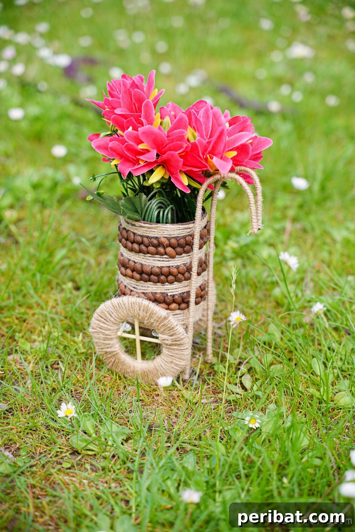 Upcycled tin can vase wrapped in twine and accented with coffee beans, holding pink flowers on green grass.