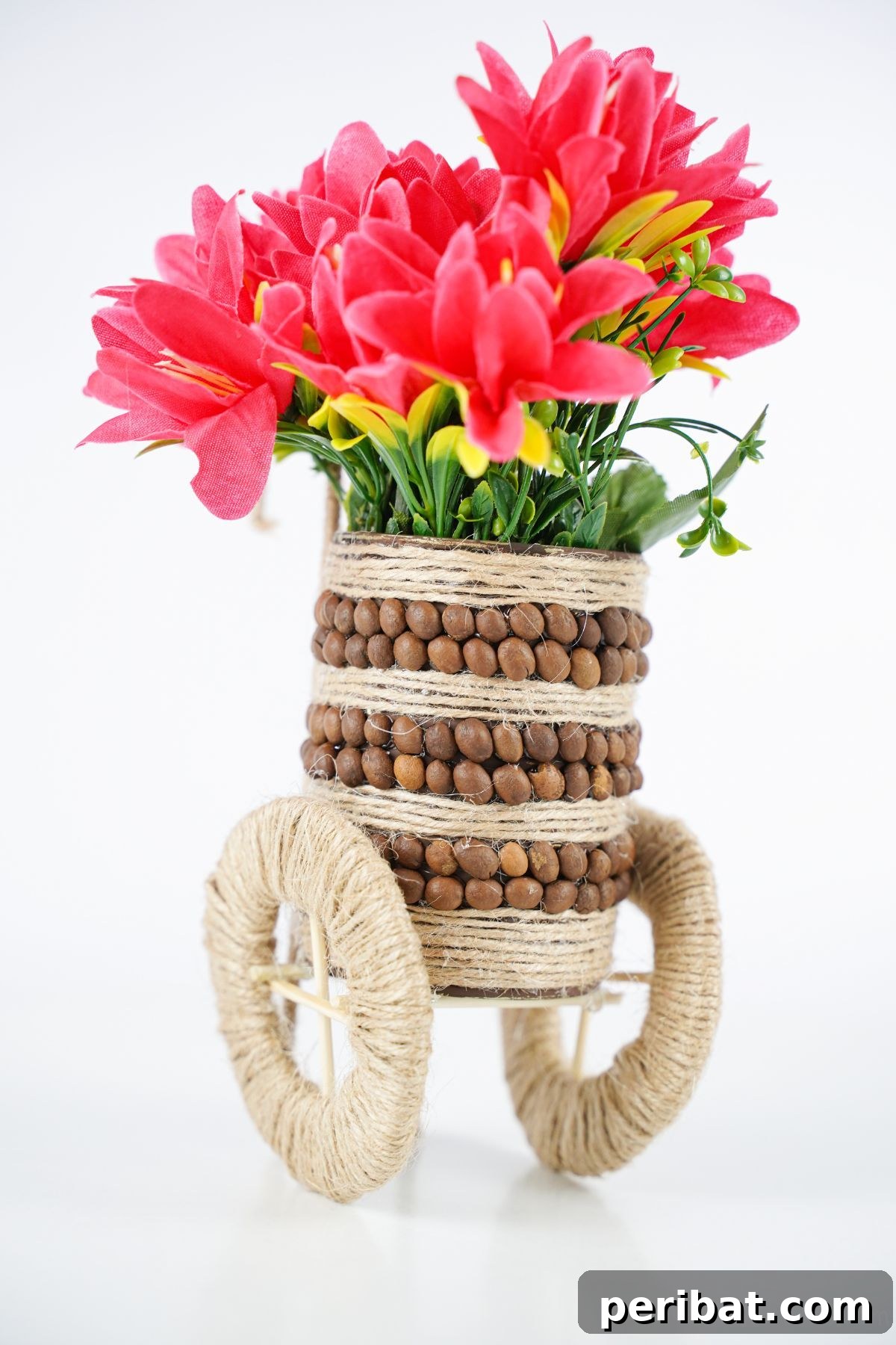 Charming tin can vase, decorated with twine and coffee beans, showcasing pink flowers on a white table.