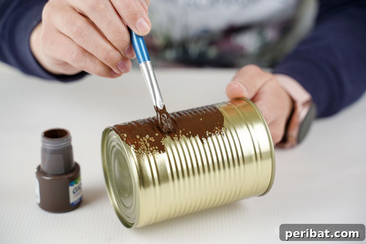 Hand carefully painting a tin can brown, preparing it for a rustic upcycled vase project.