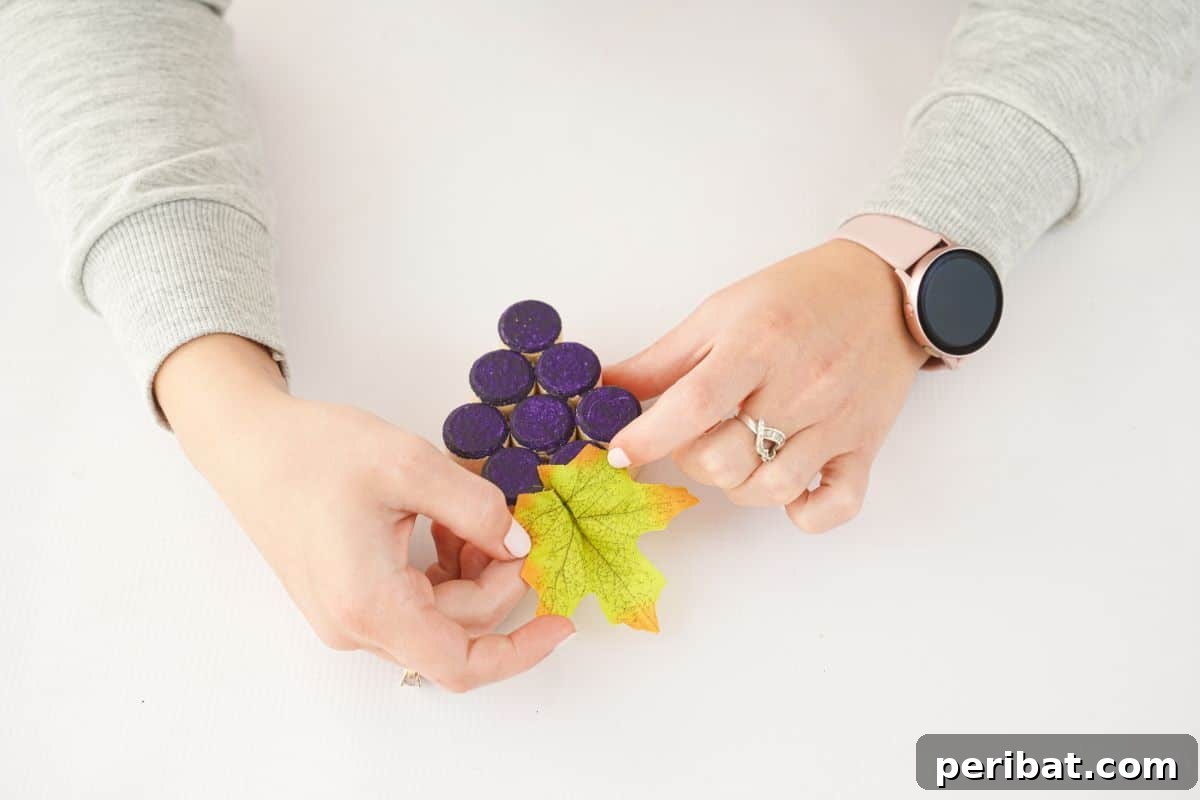 hand gluing fake green leaf on top of wine cork grape cluster