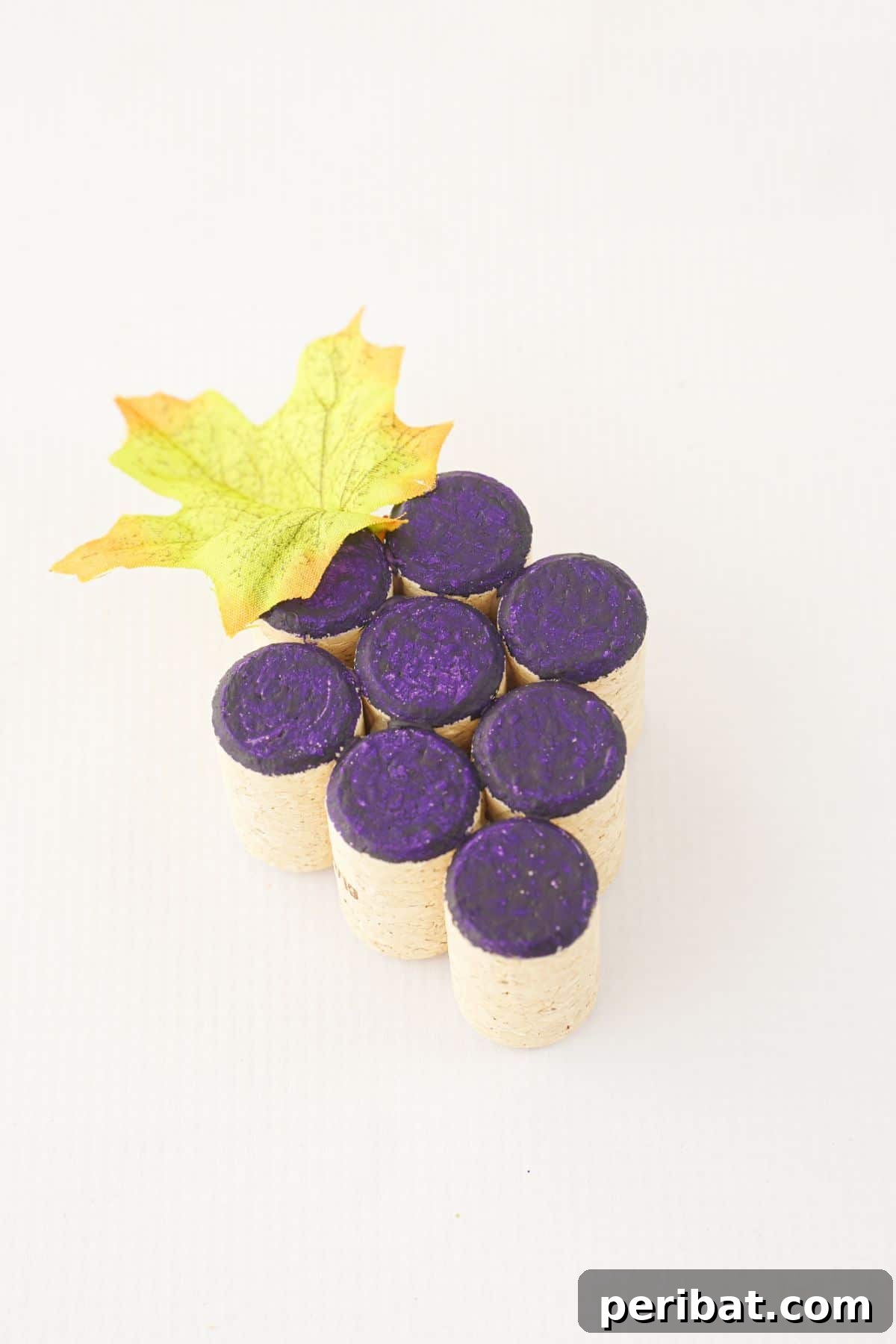 Wine cork grape cluster on a white table with leaves attached.