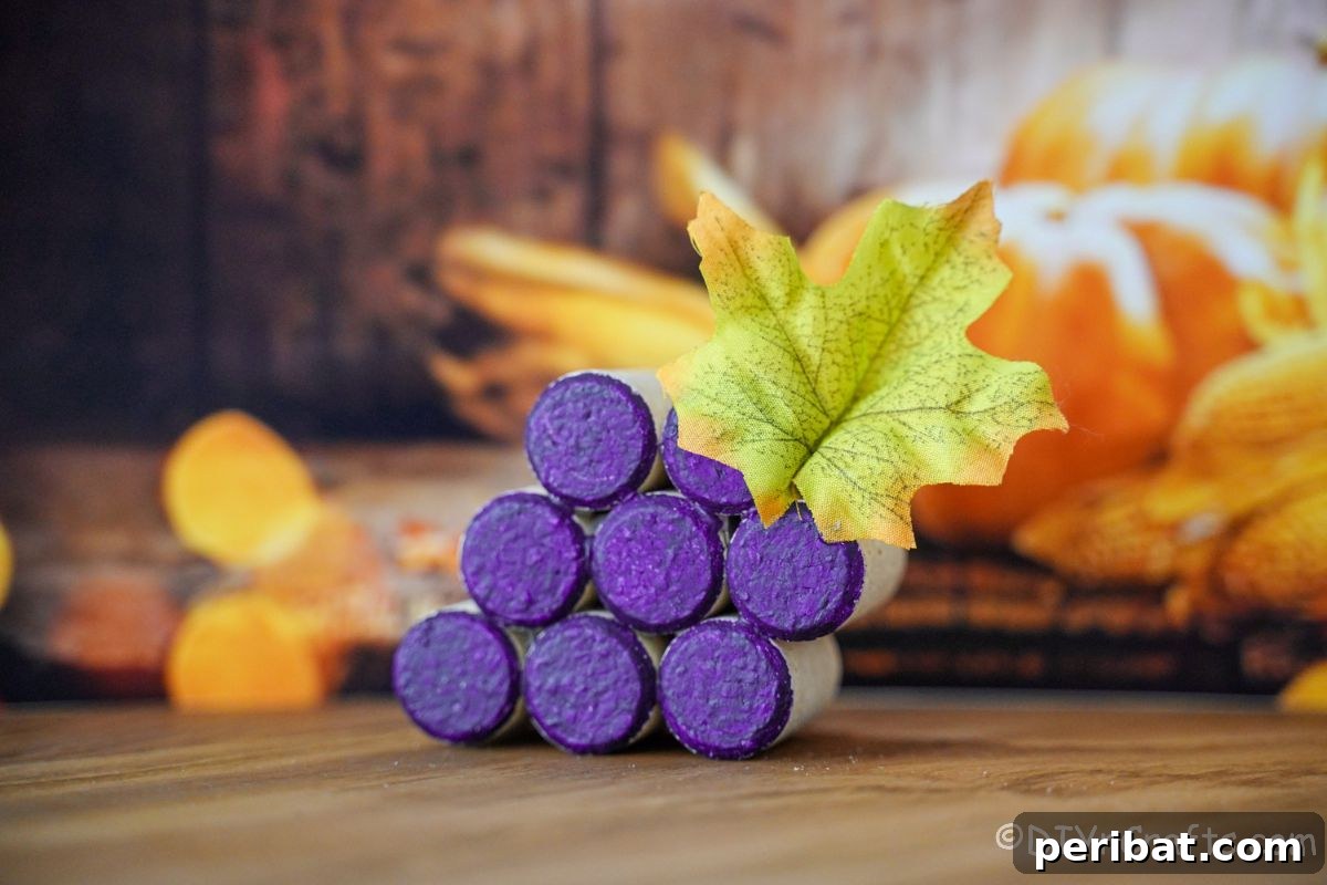 A purple wine cork grape cluster with green leaves on a table, surrounded by artificial fall leaves.