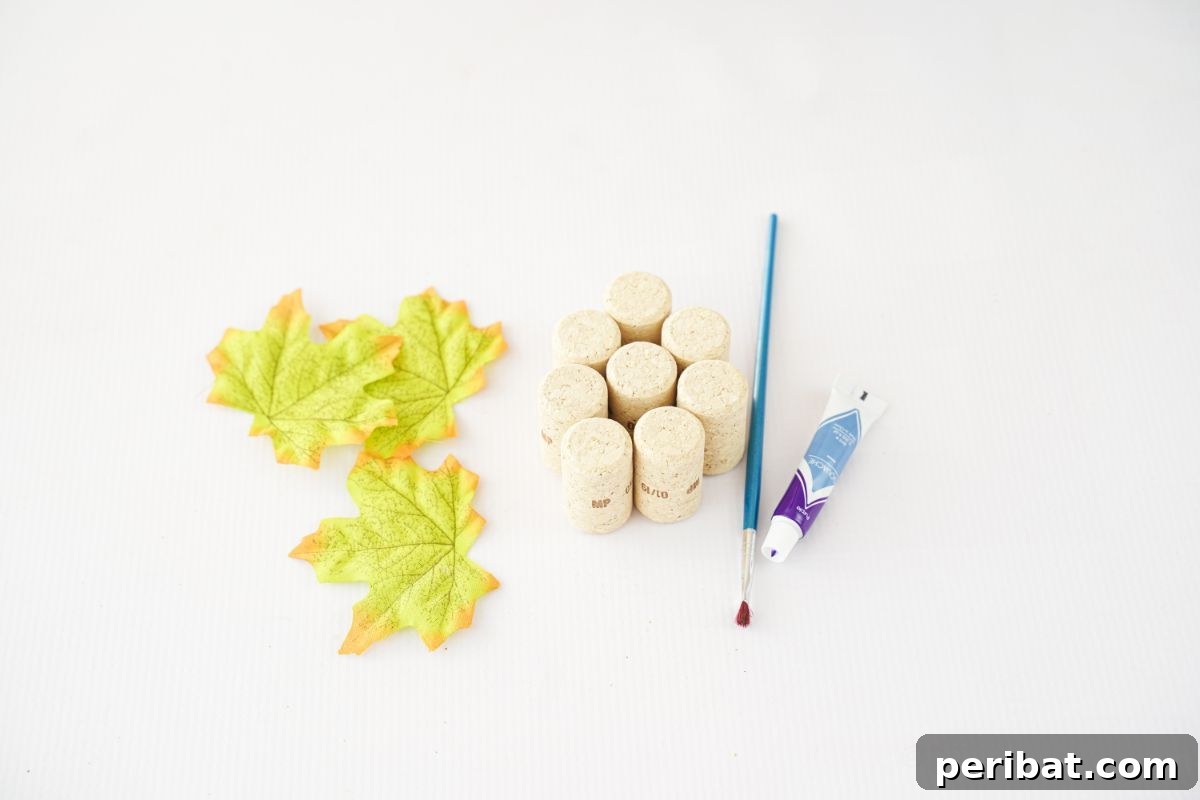 Fake leaves, wine corks, craft paint, and a paintbrush laid out on a white table, ready for crafting.
