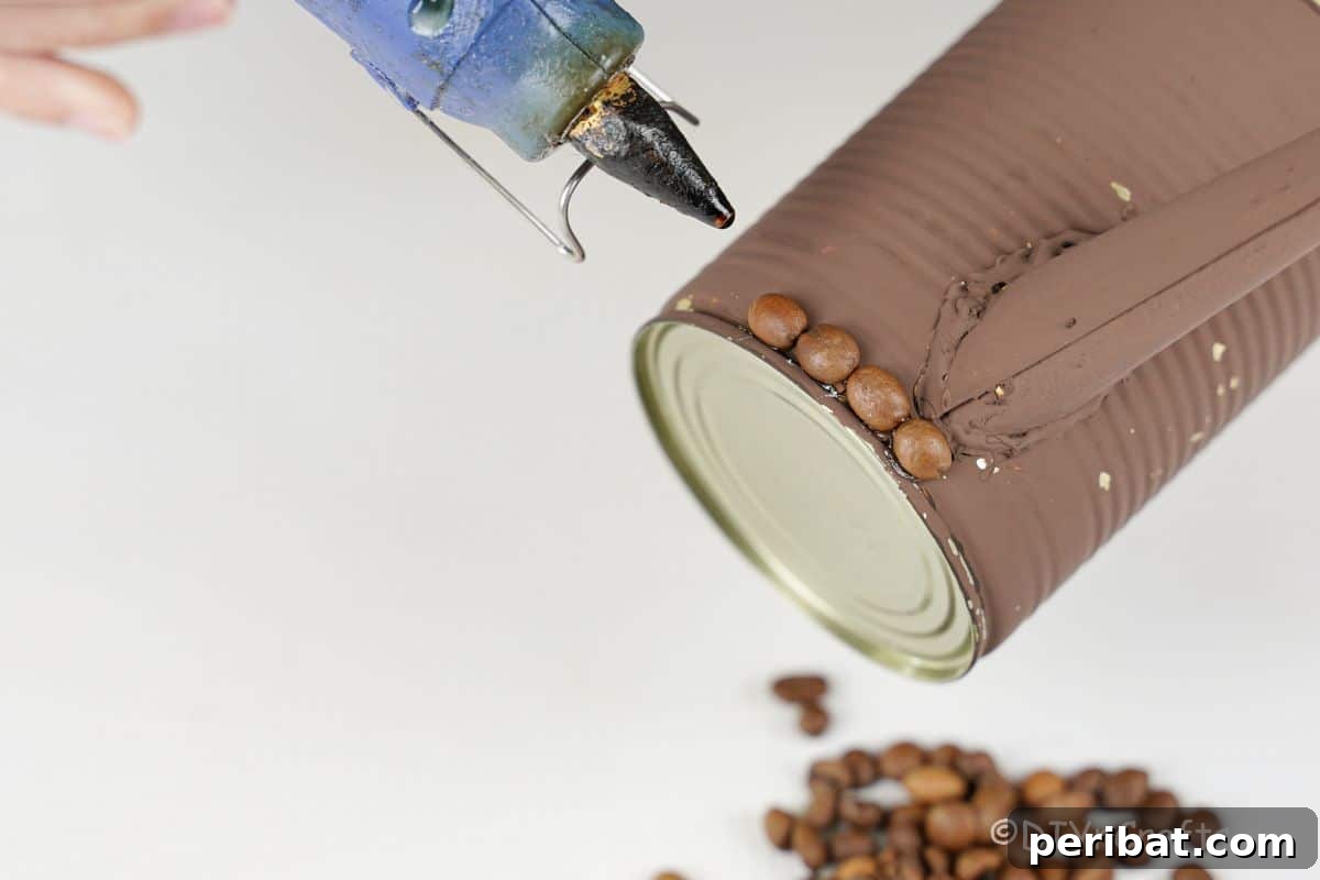 Rustic Coffee Motif Tin Watering Can 17 Hot glue gun positioned above a brown-painted tin can, ready to apply coffee beans