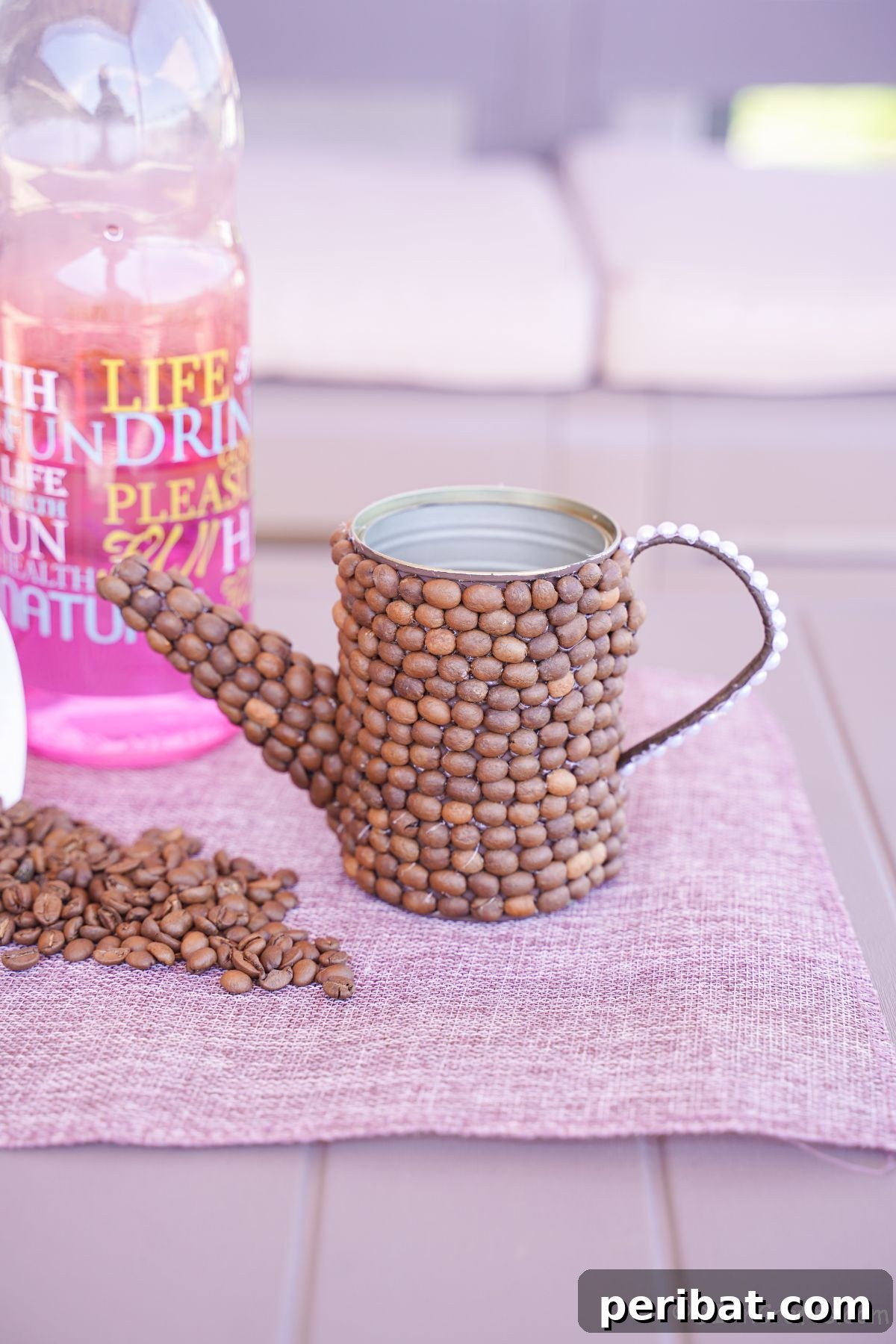 Rustic Coffee Motif Tin Watering Can 4 Decorative coffee bean covered watering can on a purple placemat next to a colorful bottle