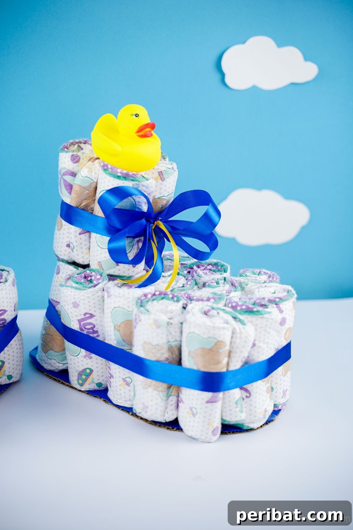 Sweet Steps Diaper Cake Delight 22 rubber ducky on top of baby bootie diaper cake with blue wall in background