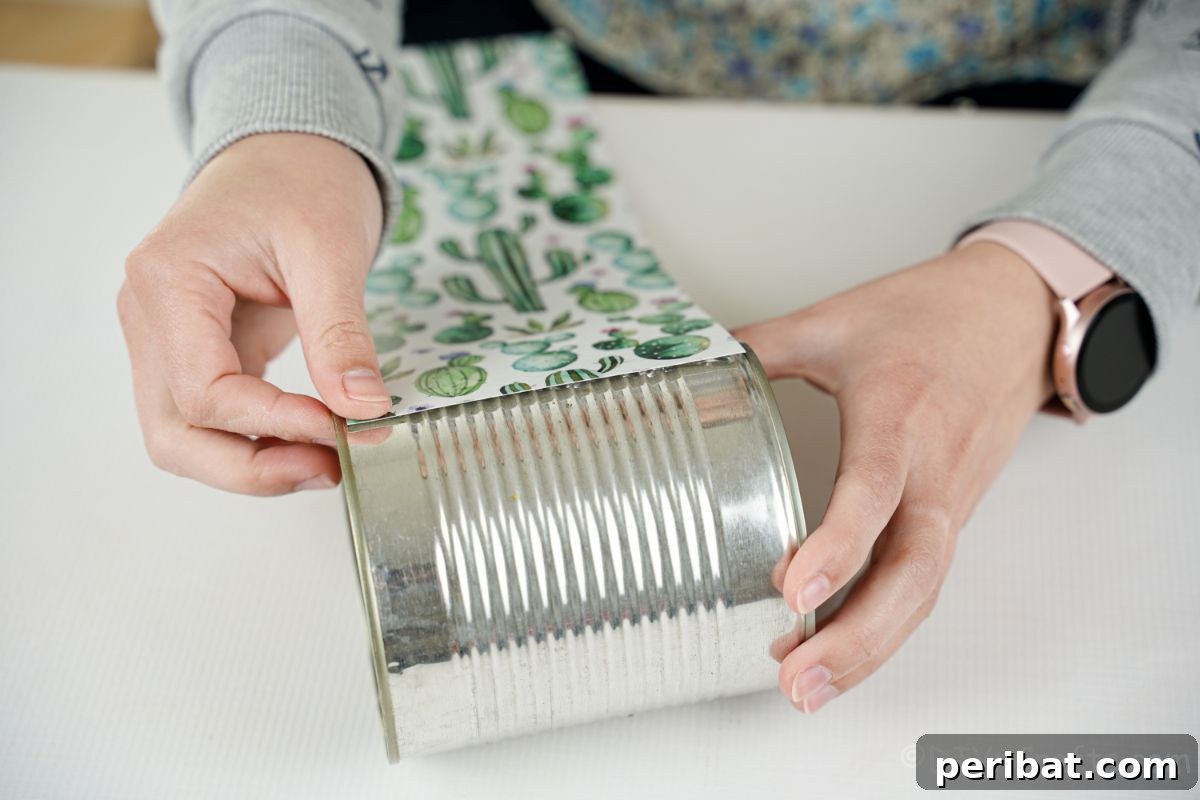 Vibrant Upcycled Tin Can Wind Socks 11 Cactus-patterned scrapbook paper being meticulously wrapped and glued around a tin can, ensuring a smooth and decorative finish.