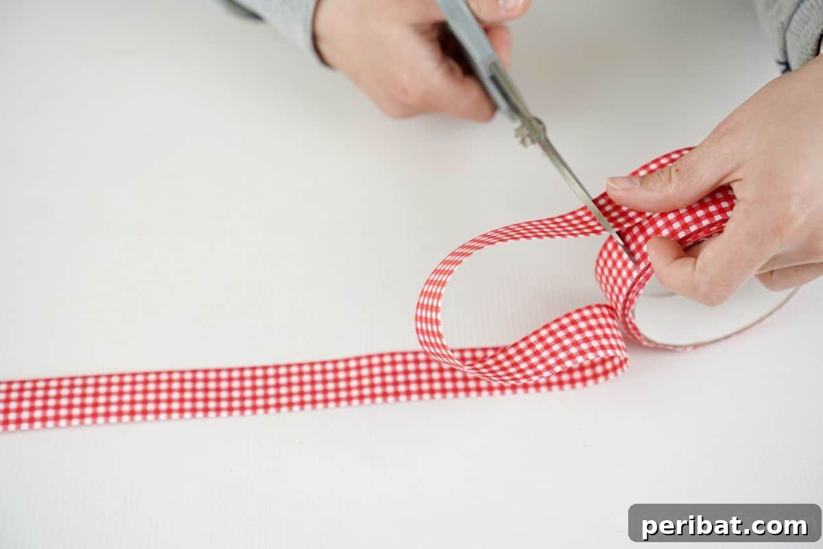 Vibrant Upcycled Tin Can Wind Socks 13 A hand skillfully cutting a vibrant red and white ribbon to the desired length, preparing it for attachment to the tin can windsock.