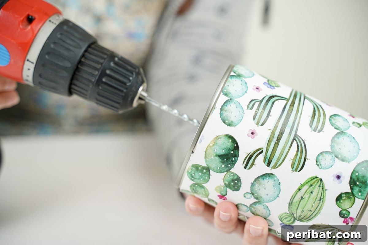 Vibrant Upcycled Tin Can Wind Socks 17 A hand operating a drill to carefully create a small hole in the closed end of a tin can, which is wrapped in cactus-patterned paper.