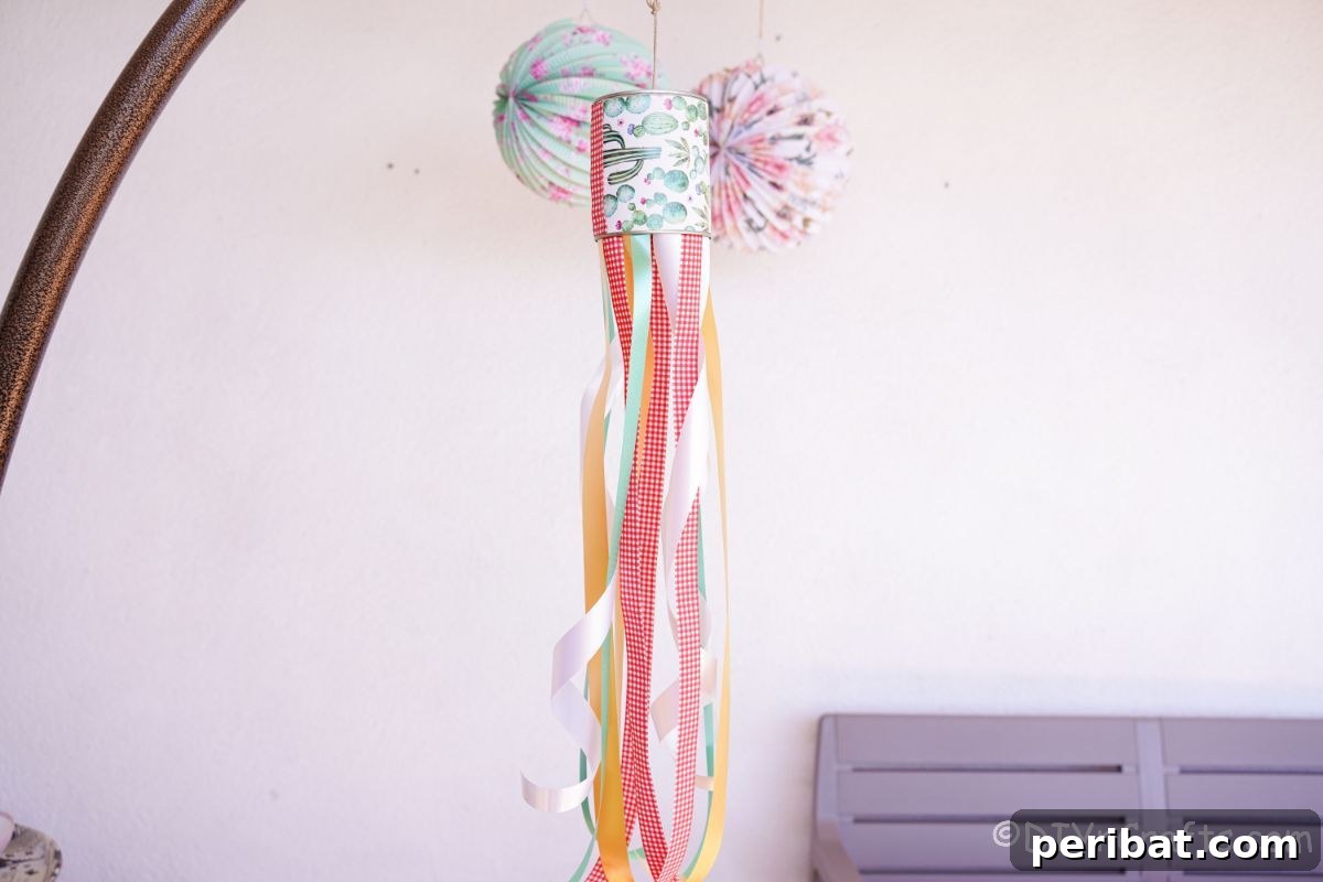 Vibrant Upcycled Tin Can Wind Socks 3 A charming tin can windsock with green, red, and yellow ribbons, gently swaying as it hangs from a deck ceiling, bringing color to the outdoor space.