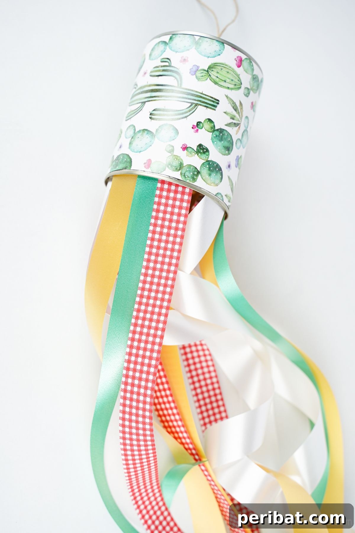 Vibrant Upcycled Tin Can Wind Socks 4 A beautifully decorated tin can windsock with an array of colorful ribbons cascading from its base, resting on a table, ready to adorn any outdoor space.