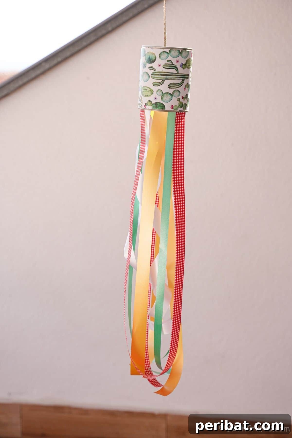 Vibrant Upcycled Tin Can Wind Socks 21 A pair of beautifully crafted windsocks, made from tin cans and adorned with different ribbon combinations, displayed against a clean white wall.