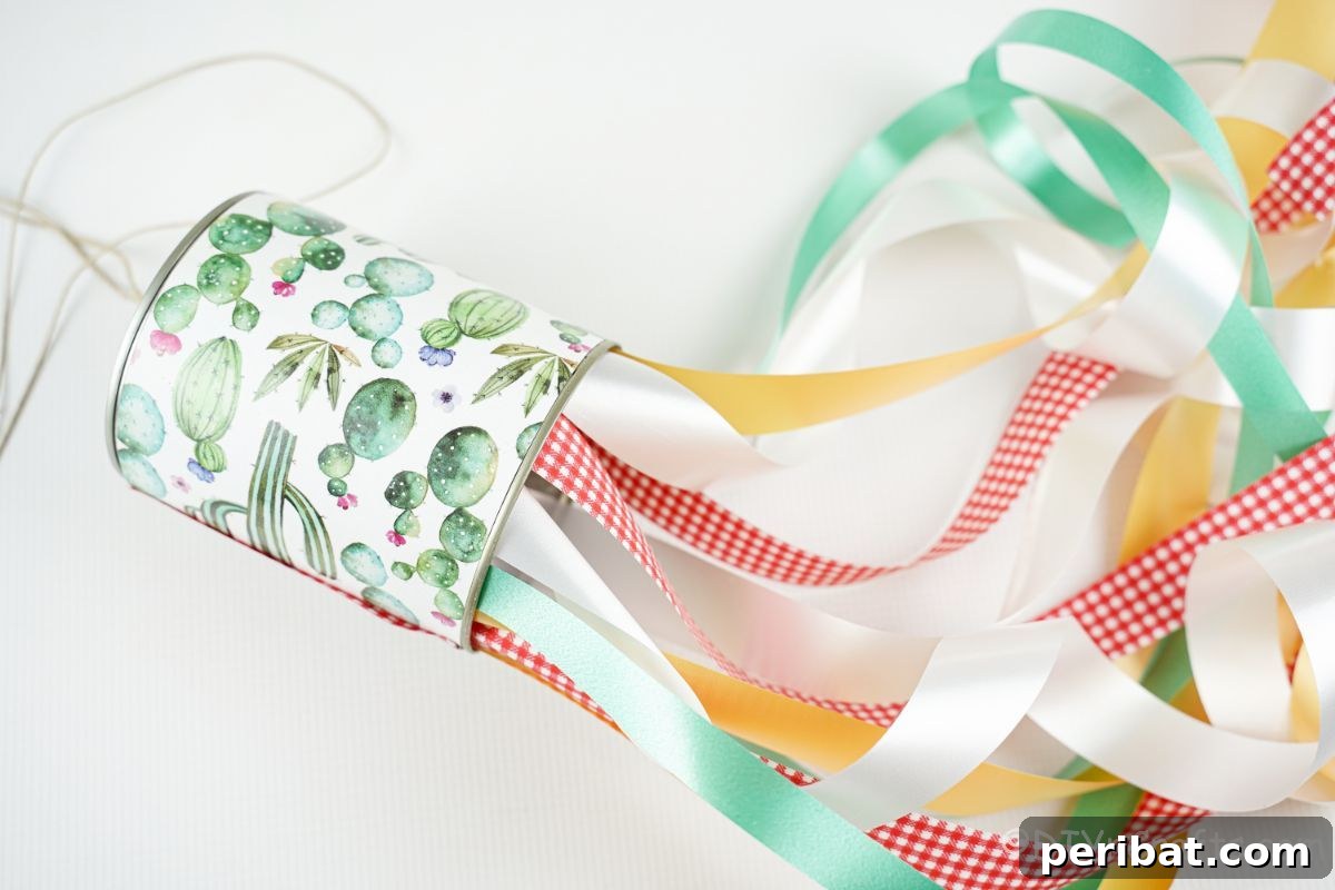 Vibrant Upcycled Tin Can Wind Socks 22 A festive tin can windsock, adorned with green, white, and yellow ribbons, rests on a white table, showcasing its simple yet charming design.