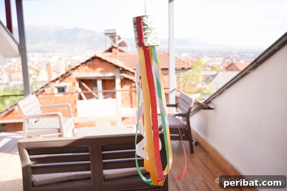 Vibrant Upcycled Tin Can Wind Socks 5 A colorful tin can windsock hanging gracefully on a sunny deck, with its ribbons flowing gently, enhancing the outdoor ambiance.