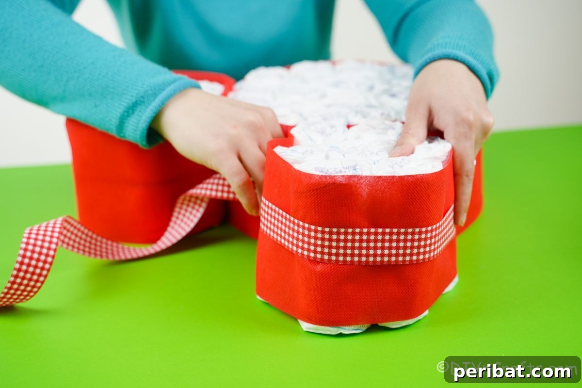 Hand carefully wrapping a red and white checked ribbon around the red-tissue-paper-covered diaper cake, adding detail.
