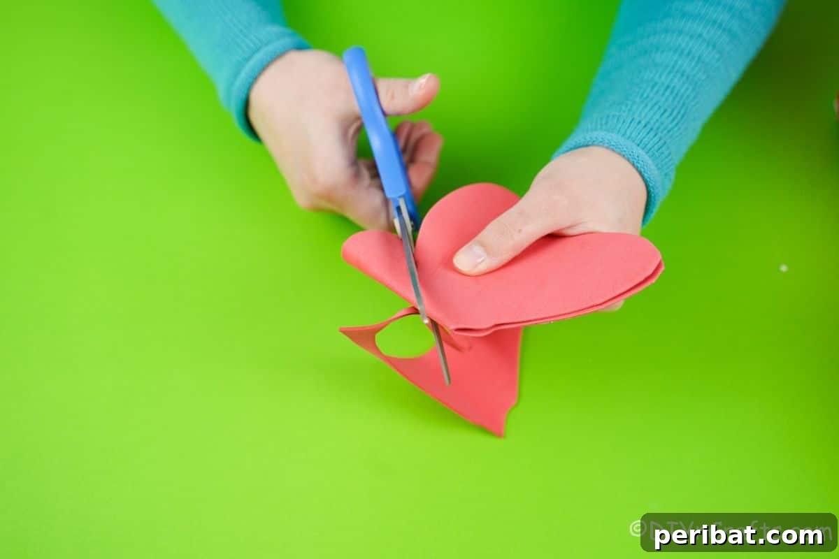 A hand precisely cutting red foam paper with blue scissors to create a bow shape, a key decorative element.