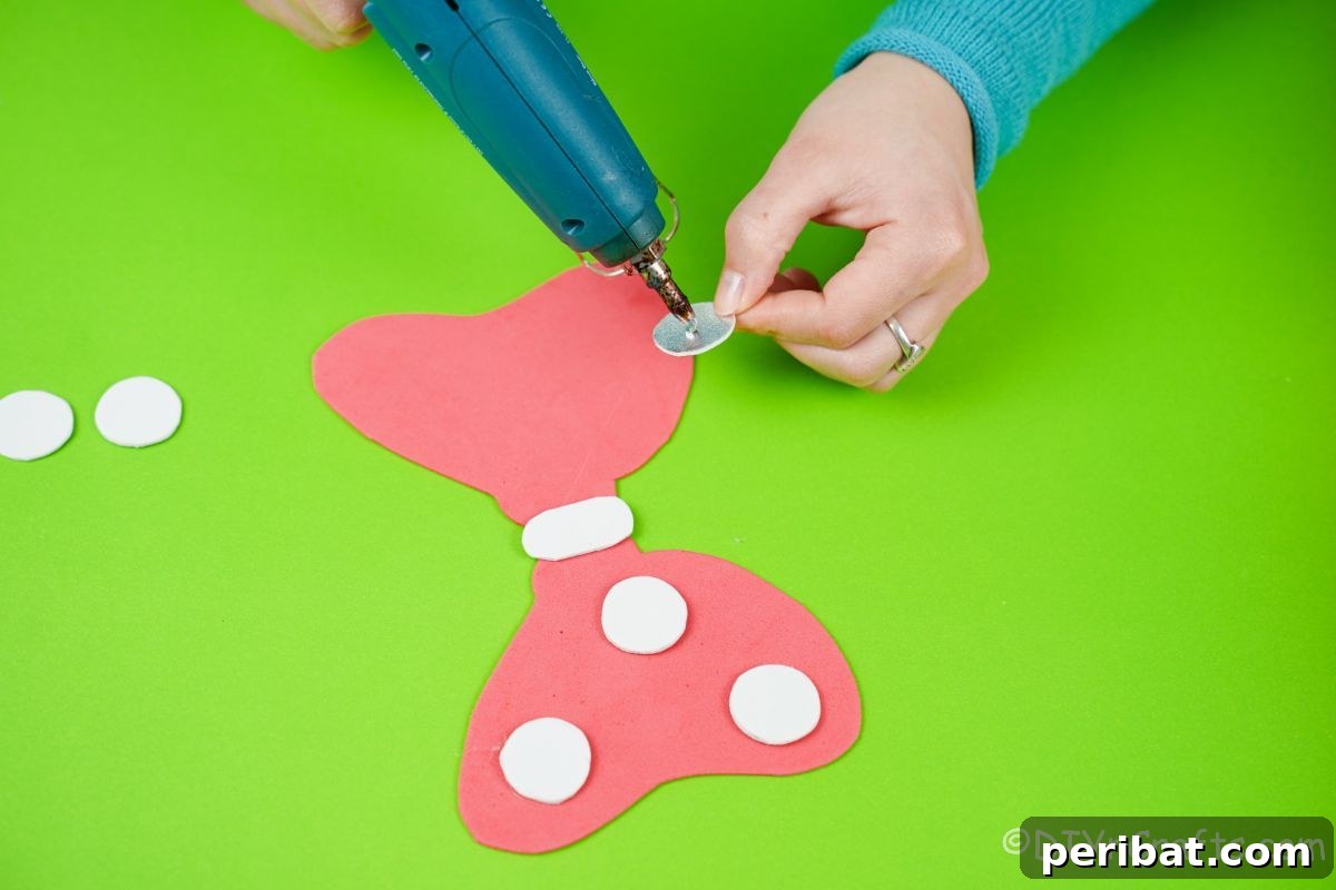 Hand gluing white circular foam pieces onto a red foam bow, illustrating the polka dot creation for Minnie Mouse.