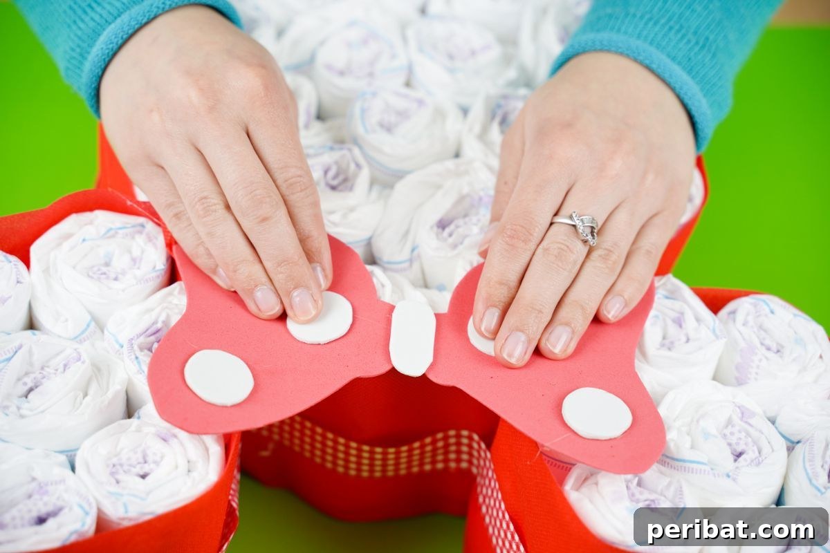 A red and white polka-dotted bow being gently placed and attached to the Minnie Mouse diaper cake head.