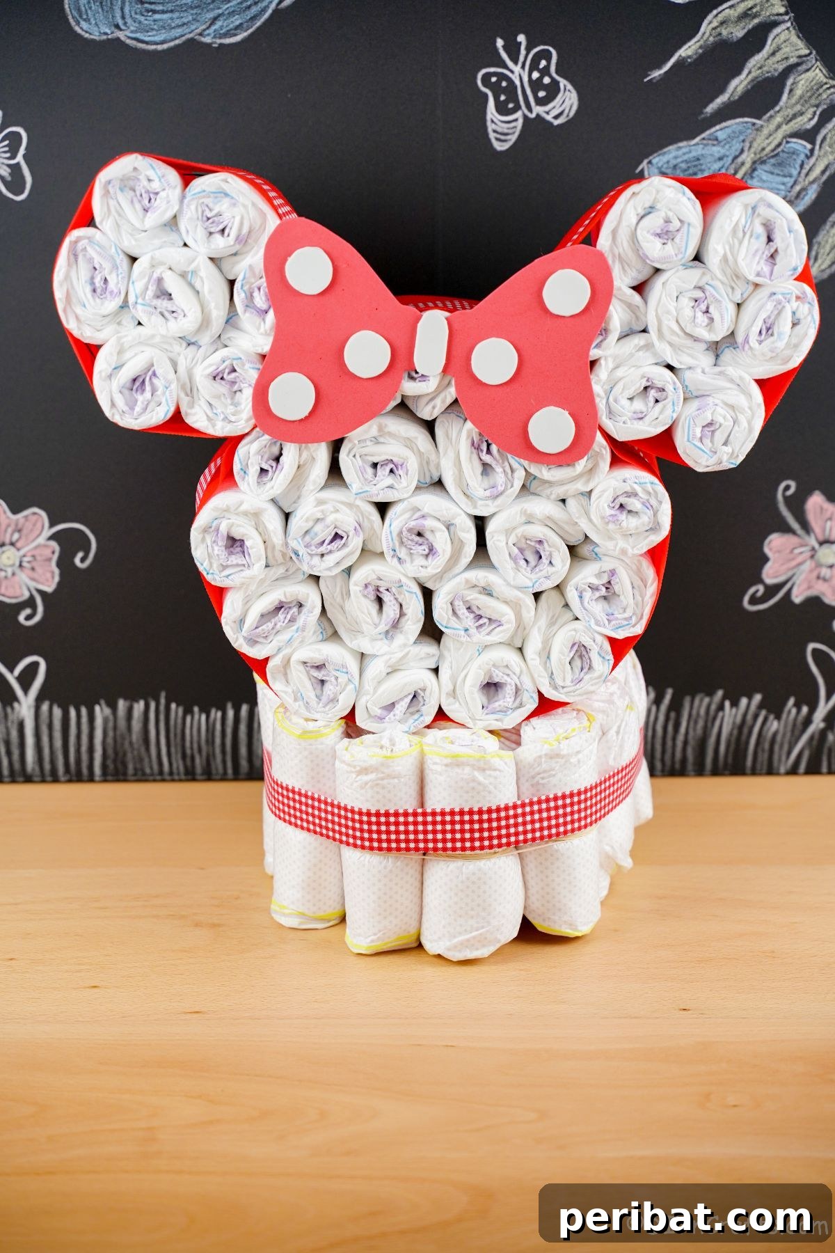 Disney Minnie Mouse head diaper cake positioned on a stylish table, with a rustic chalkboard background adding depth to the display.