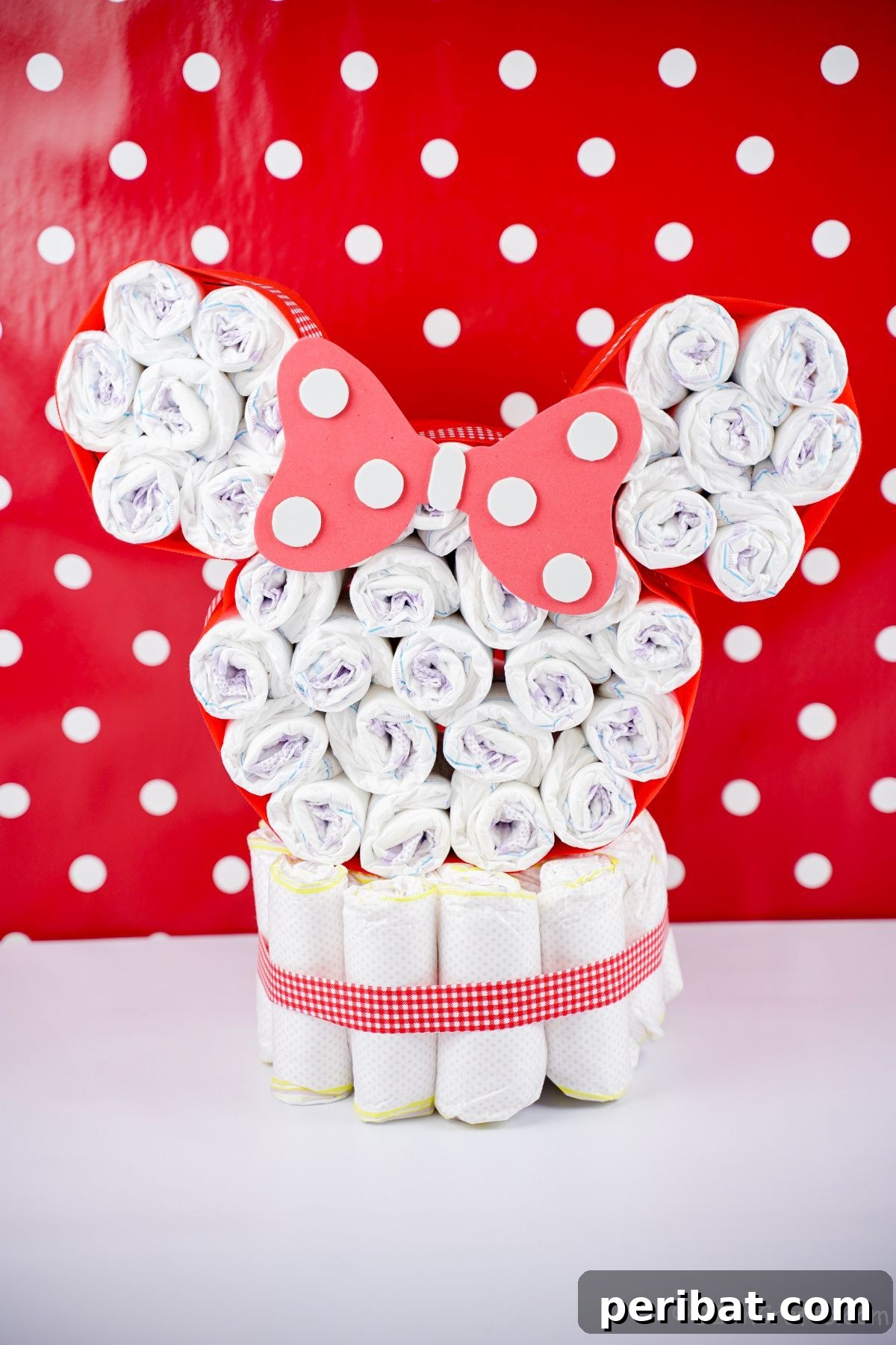 A beautifully crafted Minnie Mouse diaper cake displayed against a cheerful red and white polka dot wall, adding to its whimsical charm.