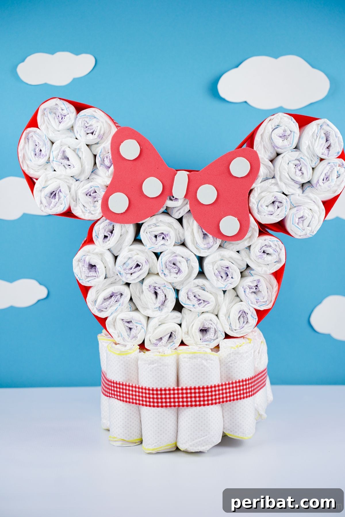 A beautifully crafted Disney Minnie Mouse diaper cake stands tall against a soft white and blue wall, ready for display.
