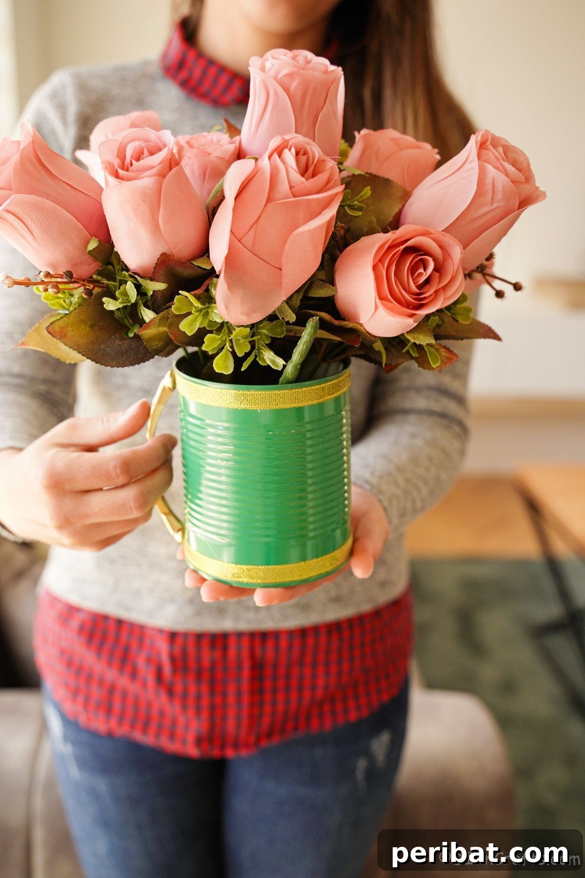 lady in grey sweater with red plaid shirt holding green tin can with pink flowers