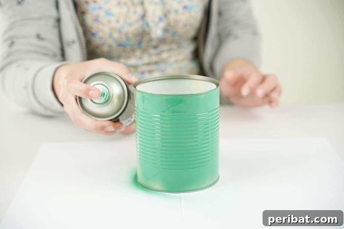 hand spraying green paint on tin can