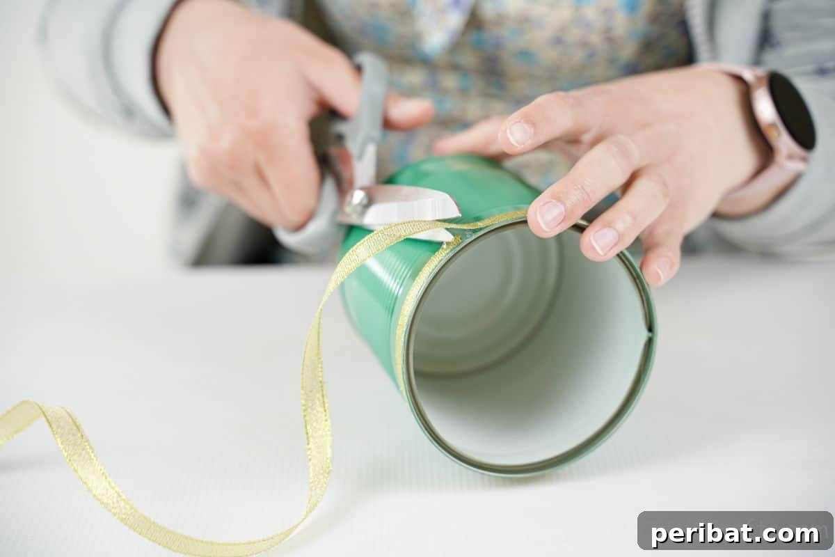 hand holding grey scissors to trim gold ribbon on green tin can