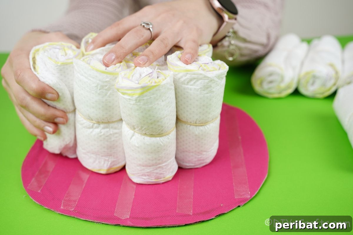 Create a Magical Unicorn Diaper Cake 11 Hand placing rolled diapers onto a pink base to form the first tier of the diaper cake