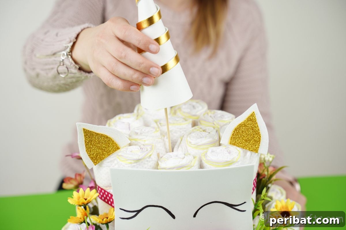 Create a Magical Unicorn Diaper Cake 21 Lady adding a meticulously crafted unicorn horn to the top of the diaper cake