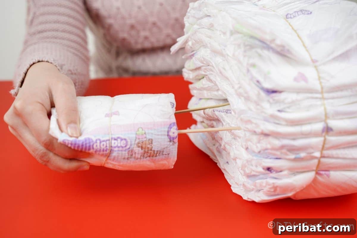 Picture Perfect Diaper Cake Camera 12 Hand inserting a diaper-wrapped bottle bundle with dowel rods into the main stack of diapers