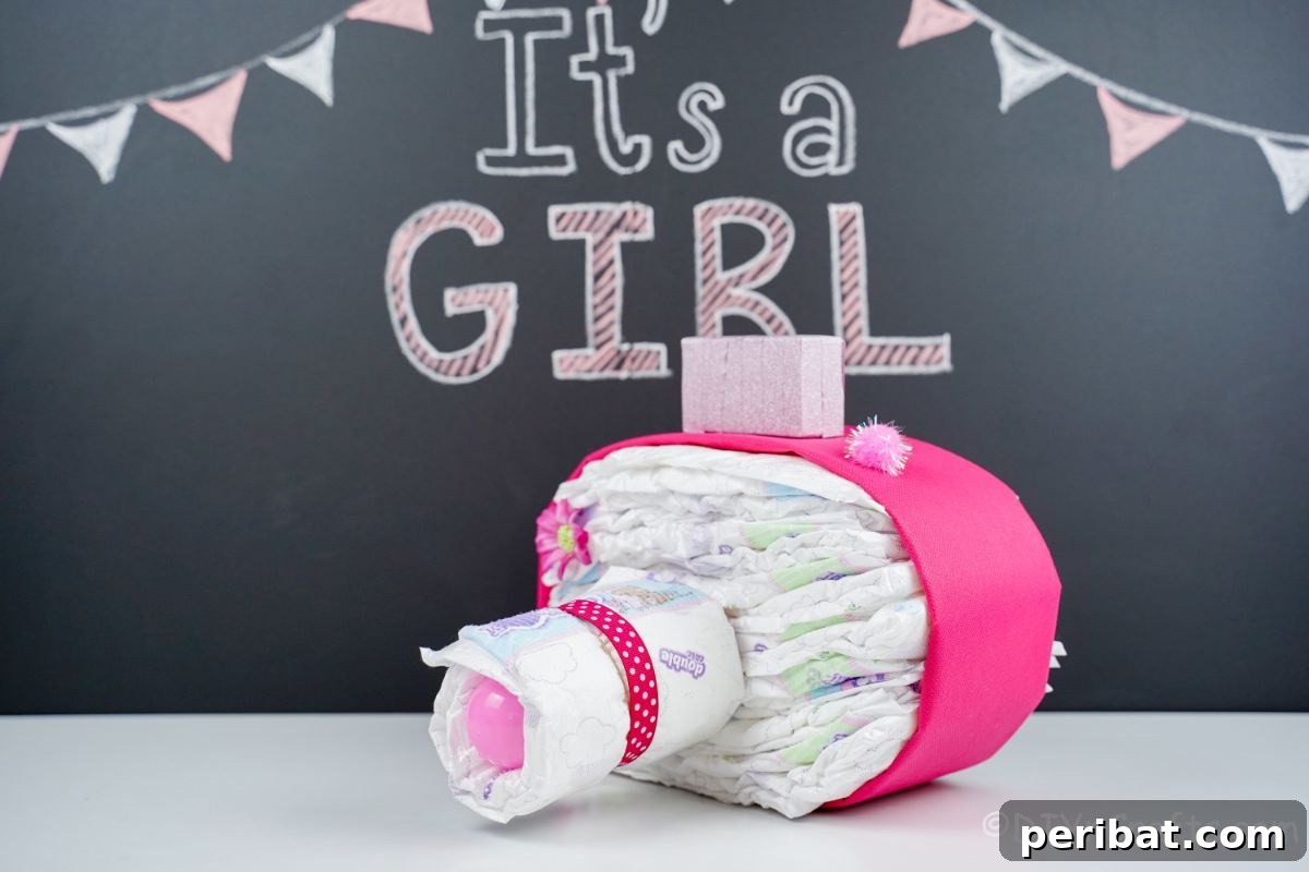 Picture Perfect Diaper Cake Camera 3 Charming pink camera diaper cake on white table with 'It's a Girl' chalkboard in background