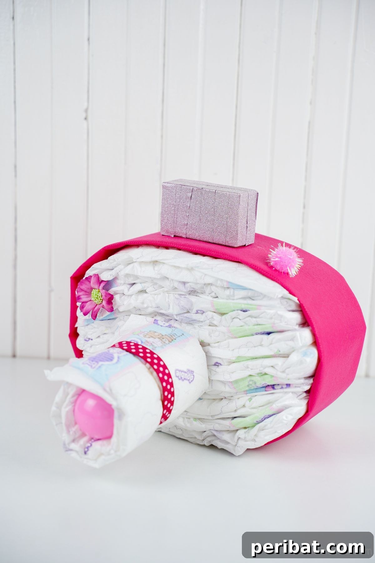 Picture Perfect Diaper Cake Camera 4 Pink camera diaper cake with delicate accents on a white table against a paneled wall