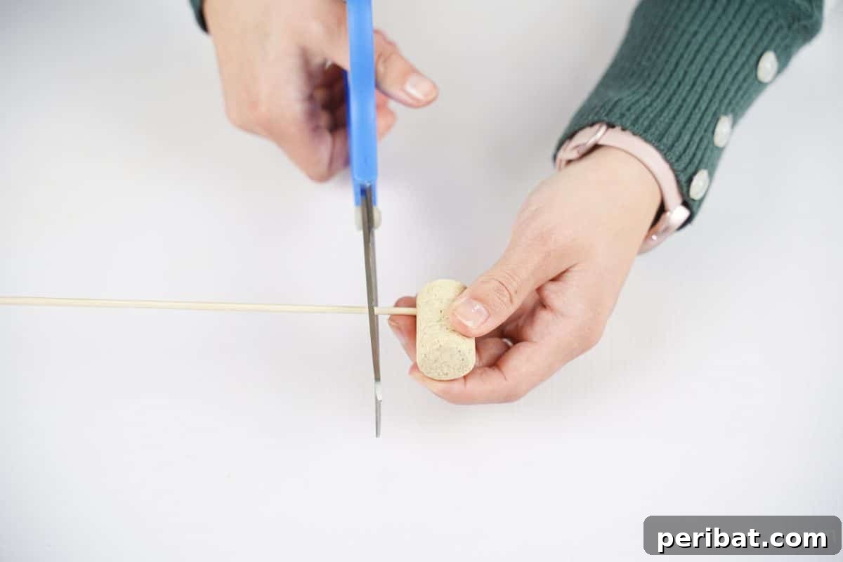 hand using blue scissors to cut dowel