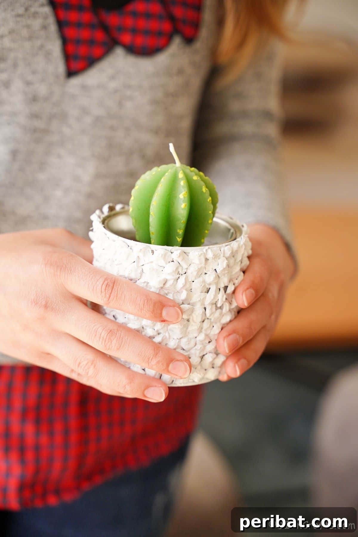 Nature-Inspired Upcycled Tin Can Planters 2 A pristine white upcycled tin can planter holding a vibrant green cactus candle, held gently in hands, showcasing its natural pinecone texture.