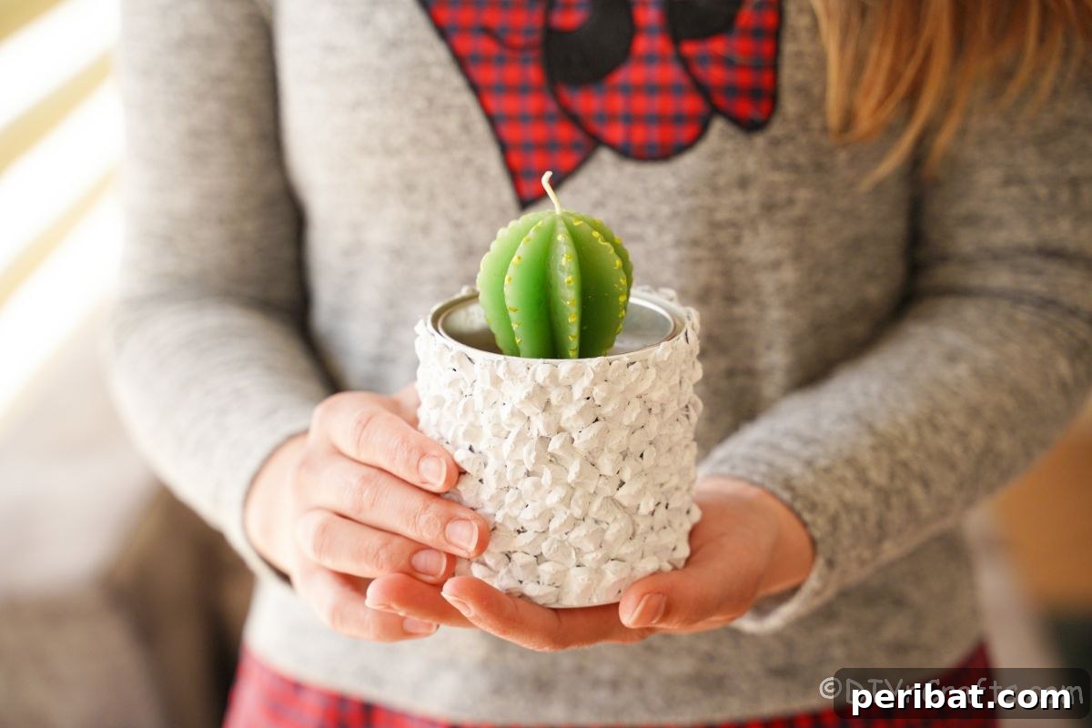 Nature-Inspired Upcycled Tin Can Planters 5 A stylish white upcycled tin can planter, containing a vibrant green cactus candle, held by a person in a grey and red sweater, highlighting its handcrafted appeal.