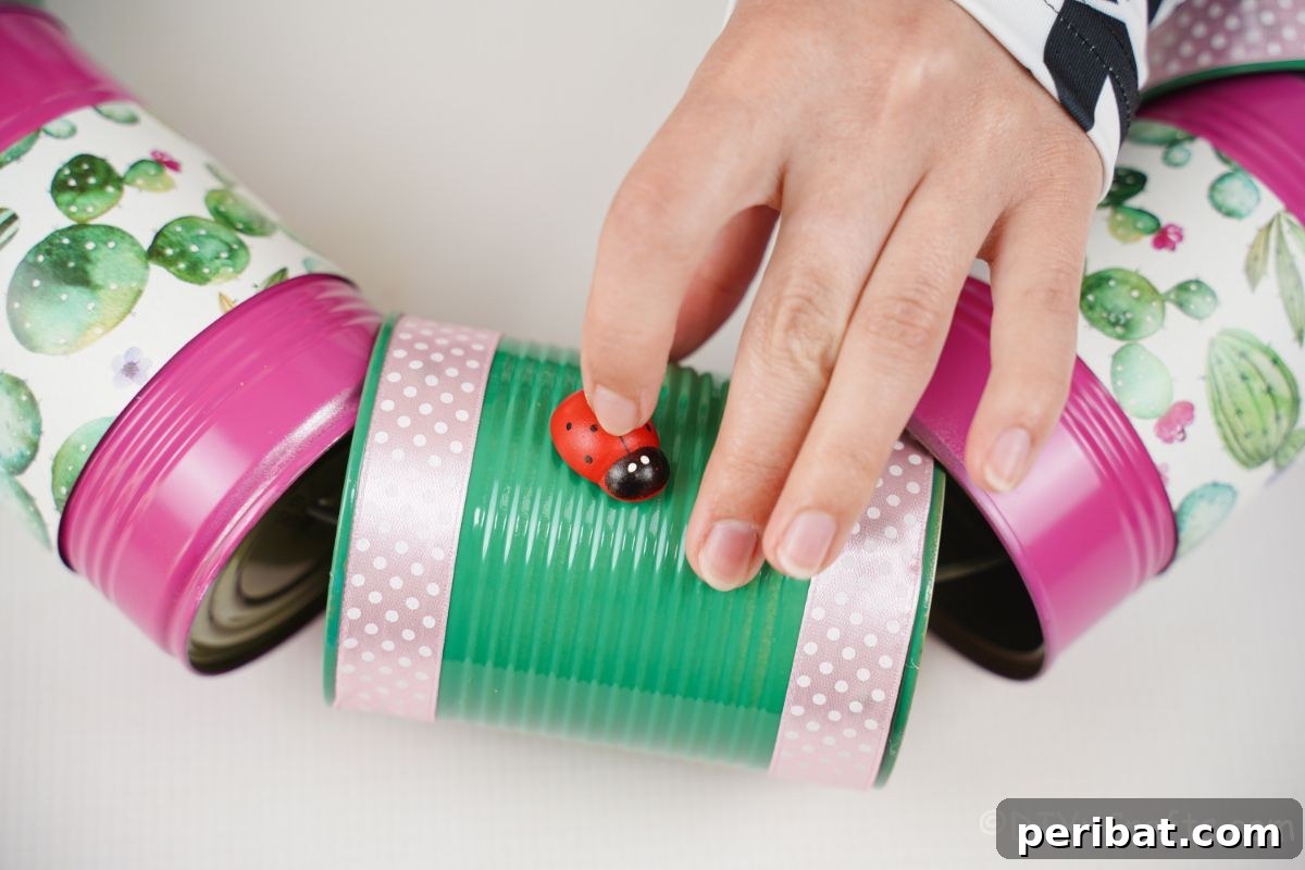 Charming Upcycled Tin Door Wreath 18 A hand gently places a small, fake ladybug onto the side of a green-painted tin can, adding a decorative touch to a craft project.
