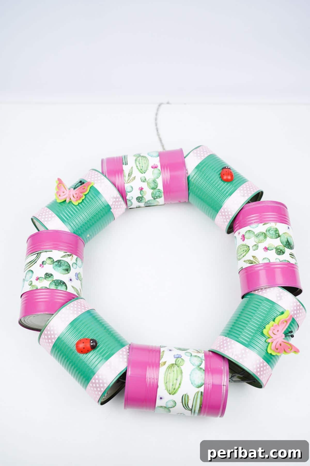 Charming Upcycled Tin Door Wreath 21 A cheerful springtime tin can wreath, made with pink and green colors, is displayed on a clean white table, showcasing its handmade charm.