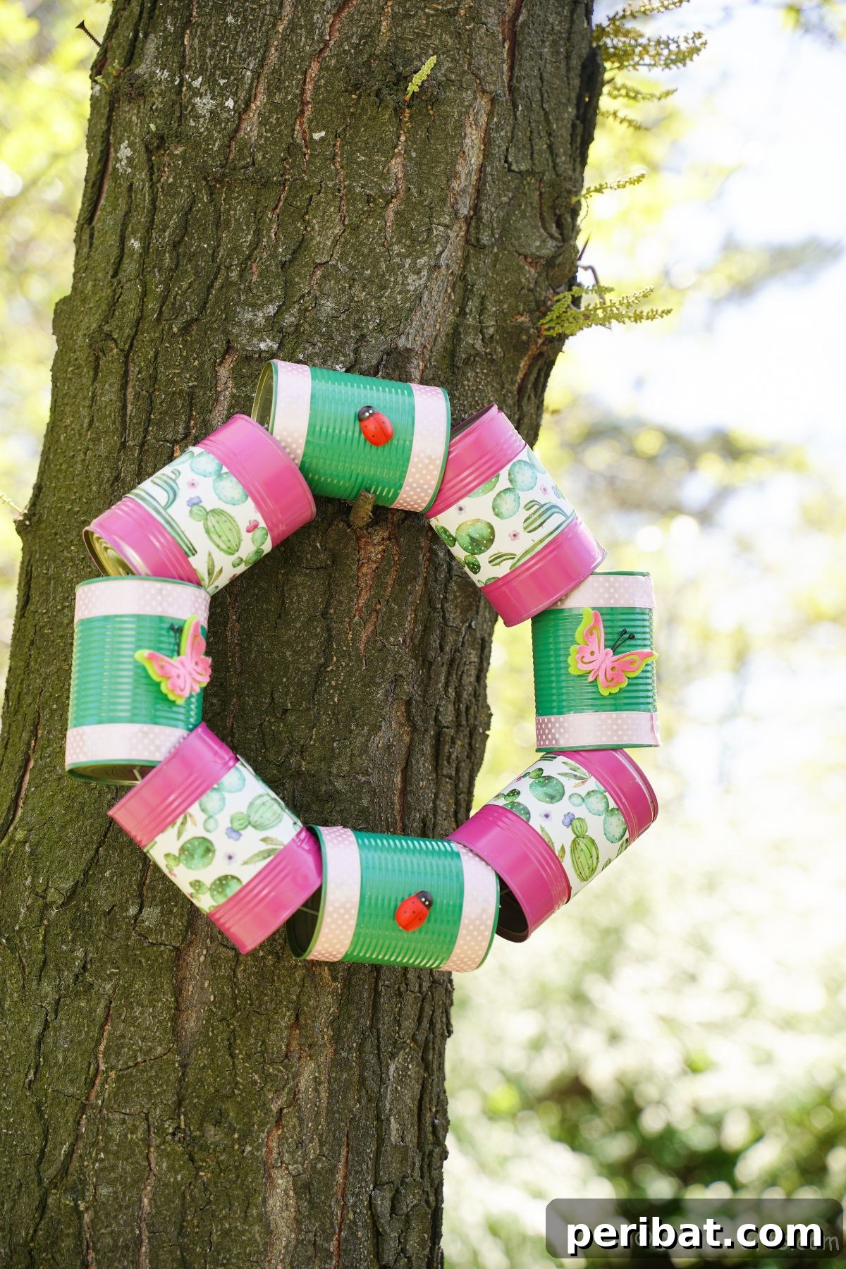 Charming Upcycled Tin Door Wreath 5 A pink and green tin can wreath is delicately hung on a rugged tree trunk, highlighting its recycled charm amidst nature.
