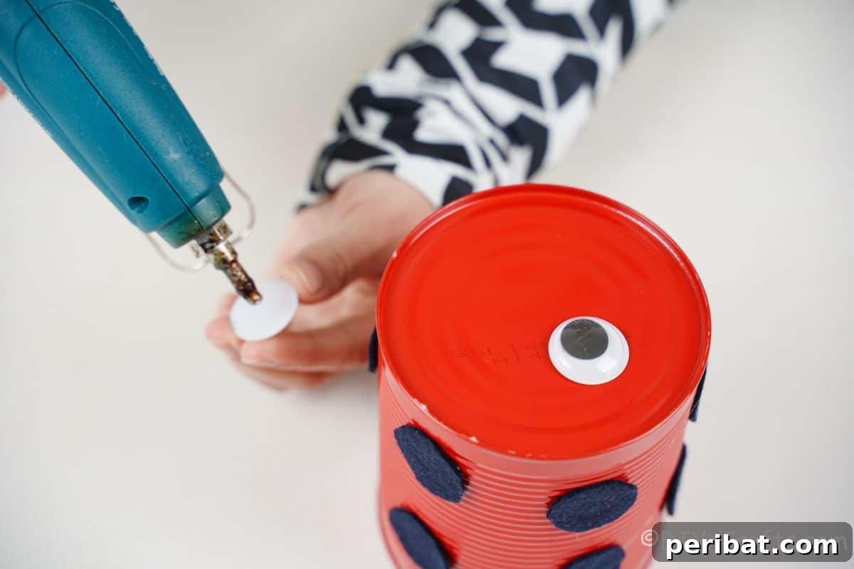 hand adding glue to googly eye for tin can