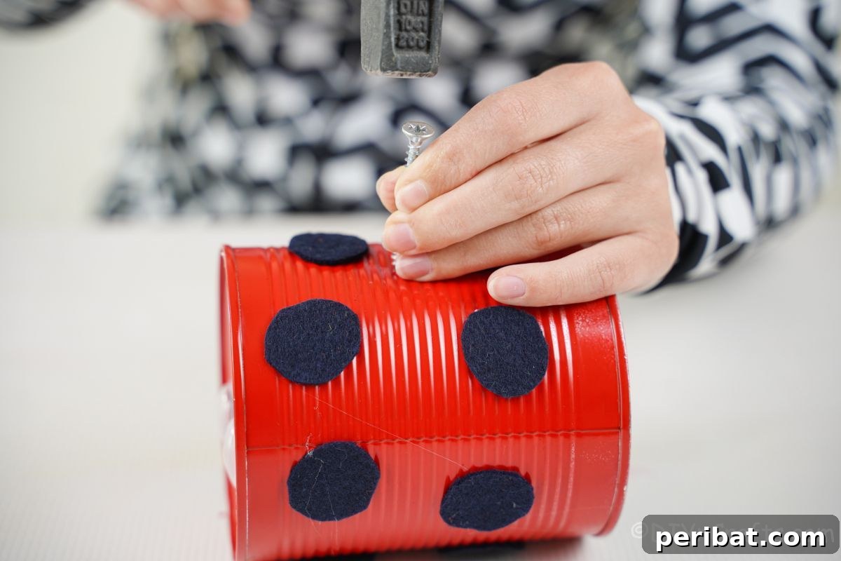hand hammering nail on top of red painted tin can