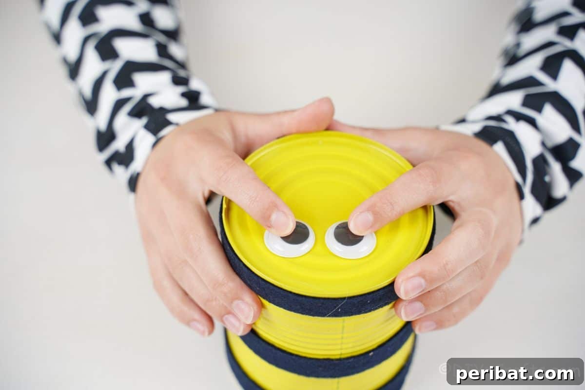 hand holding googly eyes to top of yellow tin can