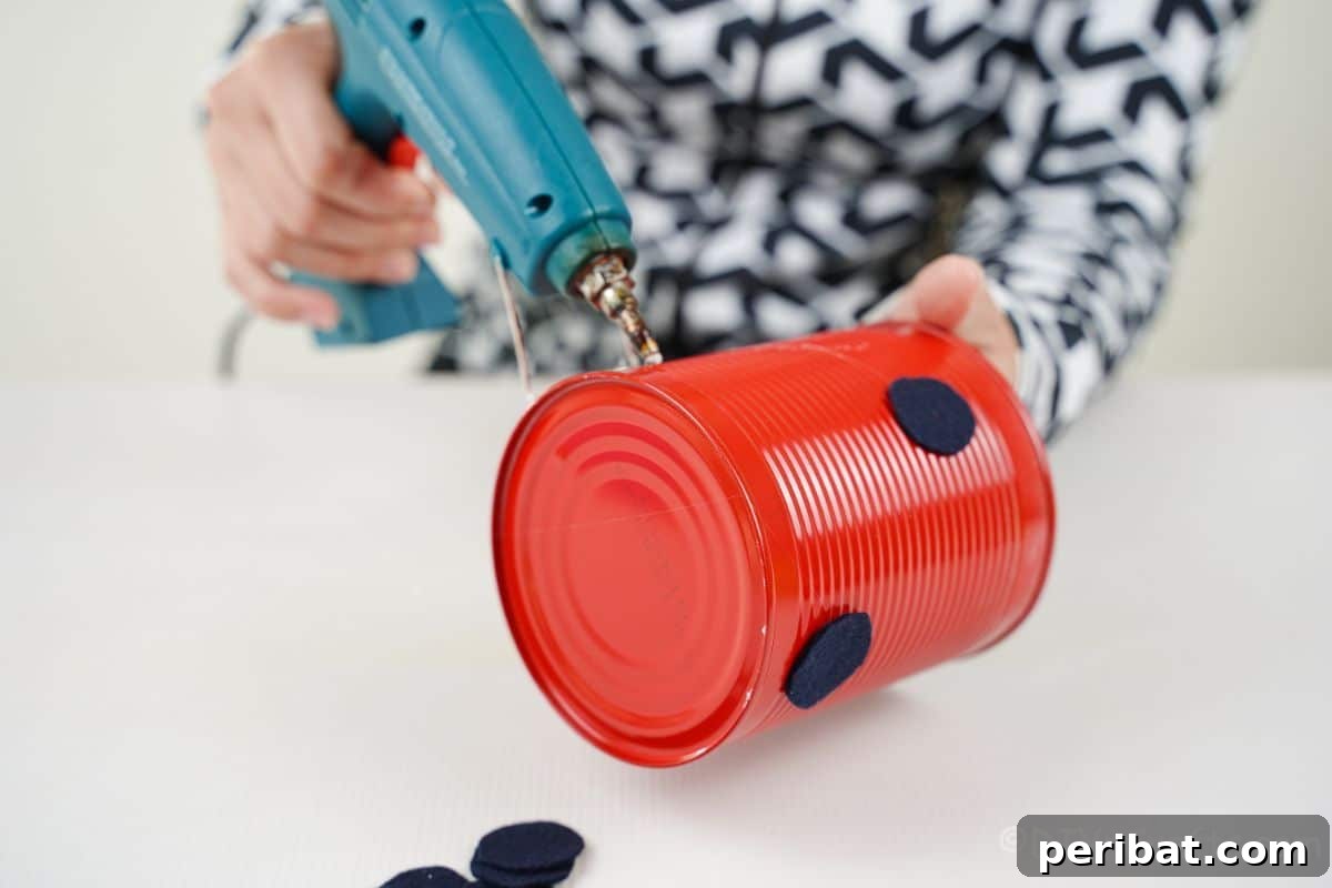glue gun holding black circles onto red tin can