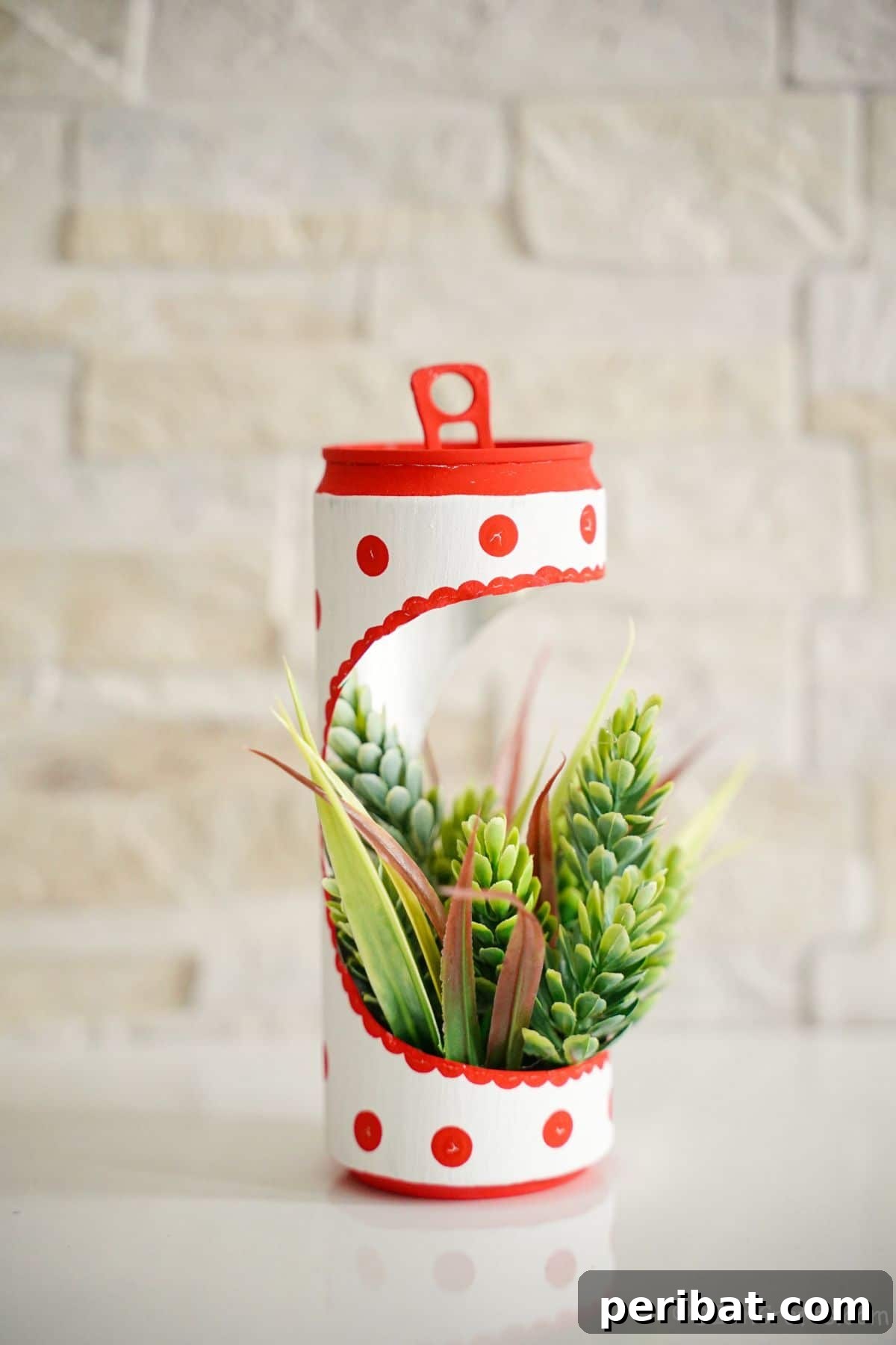 soda can planter with fake succulents on white table with cream brick wall in the background