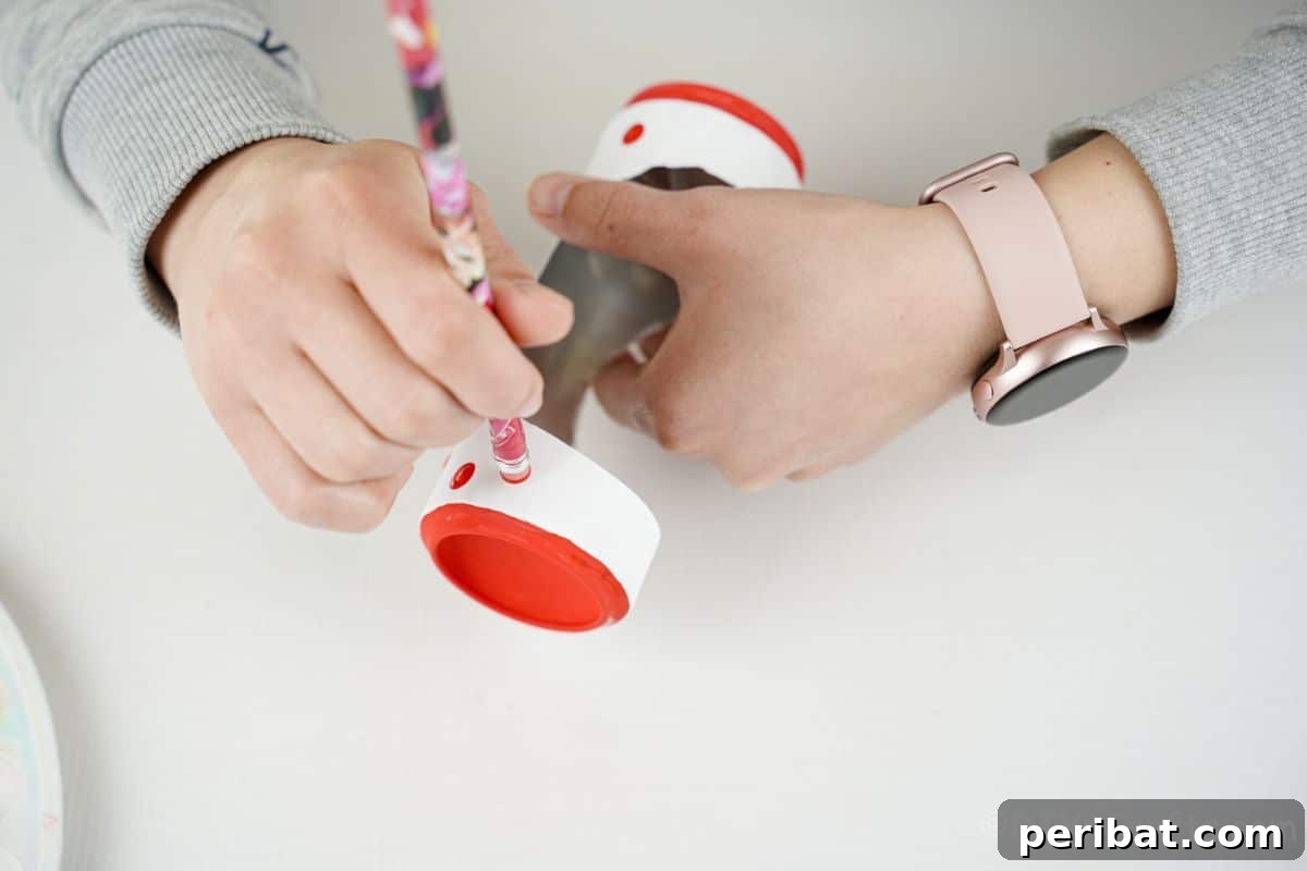 hand holding pencil to paint red dots on white can