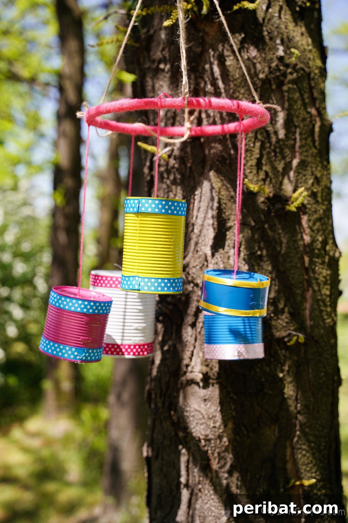 Transform Tin Cans into Melodious Wind Chimes 2 Vibrant tin can wind chime hanging gracefully on a tree, featuring pink, blue, yellow, and white colors